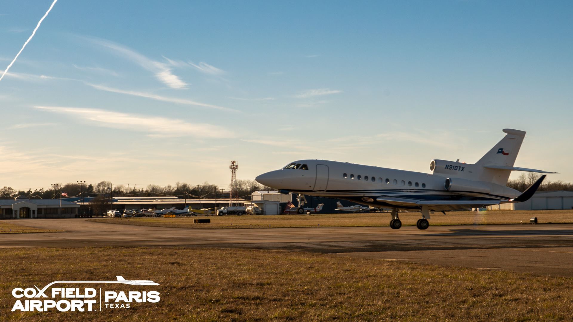 A private jet takes off from Cox Field with terminal building and hangars in background