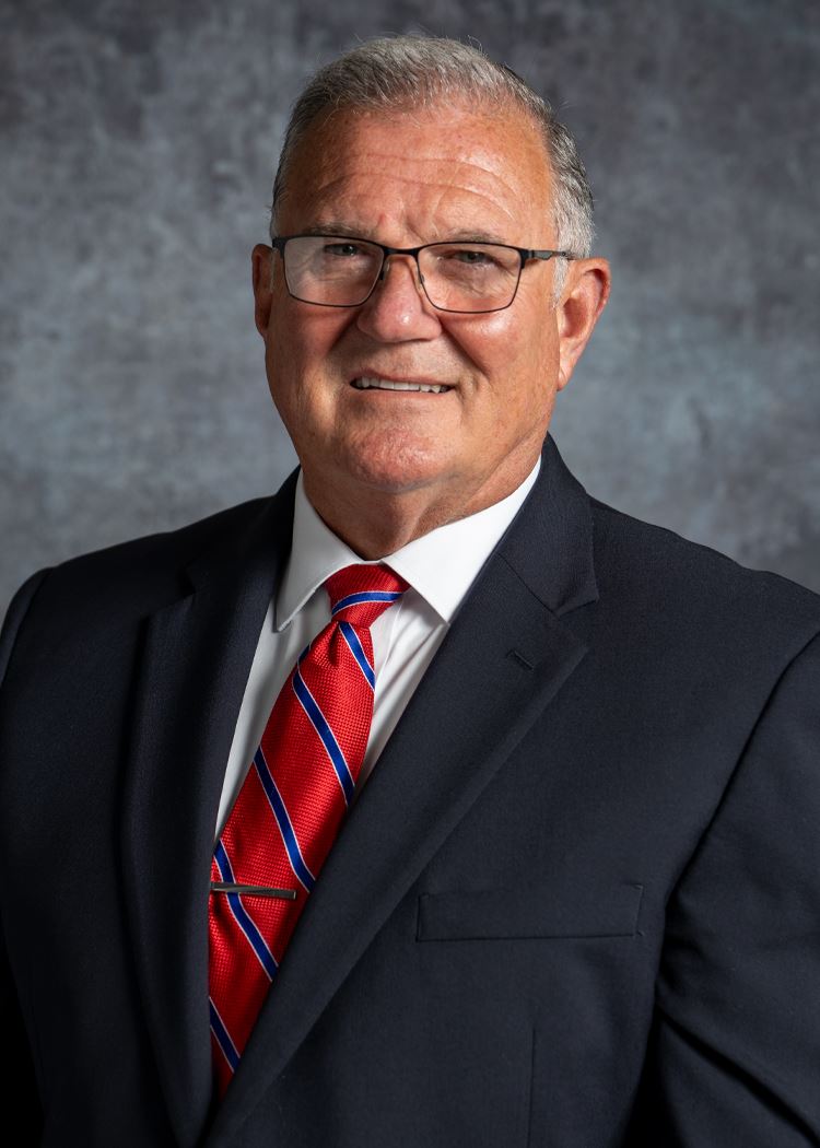 portrait of Tracy Attebury wearing red tie and navy blue sportcoat with gray backdrop 